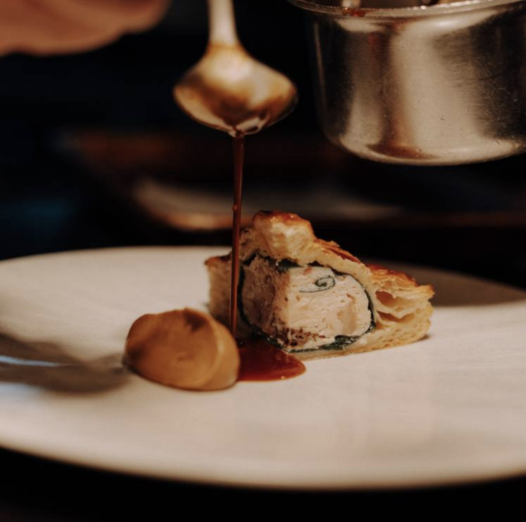 A slice of savoury pie on a while plate gets a drizzle of gravy. 